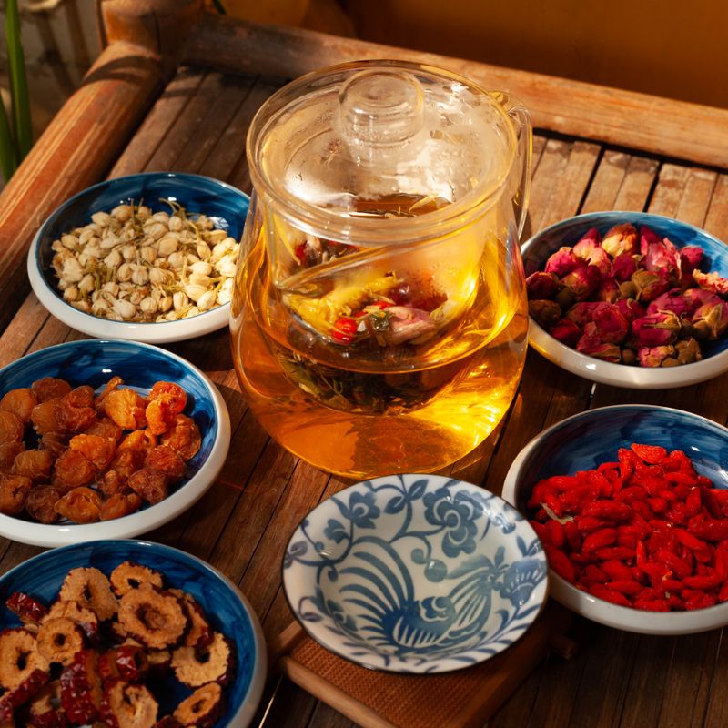 Glass teapot of herbal tea with dried flowers on a wooden tray